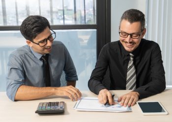 Jolly business partners discussing sales development at meeting. Happy excited businessmen examining papers and enjoying teamwork in office. Report concept