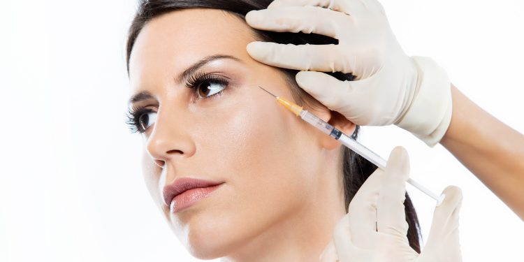 Portrait of beautiful young woman getting botox cosmetic injection in her face over white background.