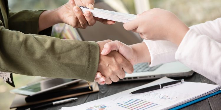 Business people shaking hands, finishing up meeting. businessman giving money to his partner while making contract - bribery and corruption concepts.