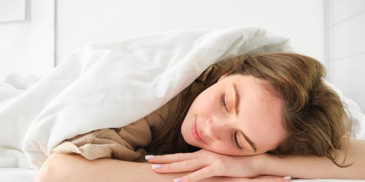 Portrait of happy young woman sleeping in her bed, enjoying a nap in hotel suite, lying under blanket.