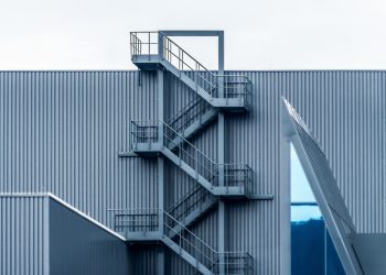 A gray metal wall with spiral stairs under the clear sky