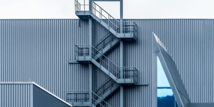 A gray metal wall with spiral stairs under the clear sky