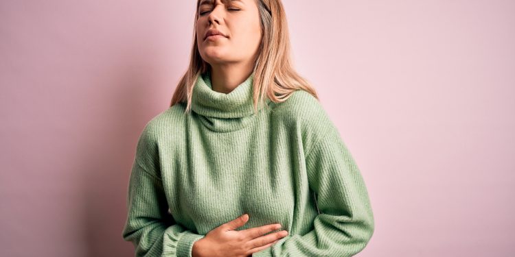 Young beautiful blonde woman wearing winter wool sweater over pink isolated background with hand on stomach because nausea, painful disease feeling unwell. Ache concept.