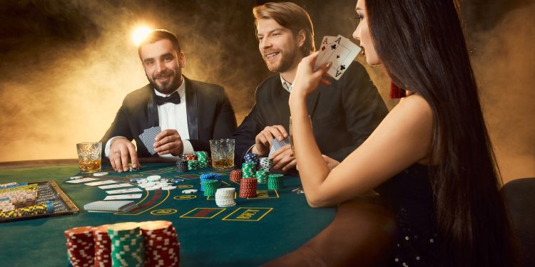 Group of young rich people is playing poker in the casino. Two men in business suits and a young woman in a black dress. Smoke. Casino. Poker