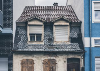 A small aged and old house between two modern and new houses