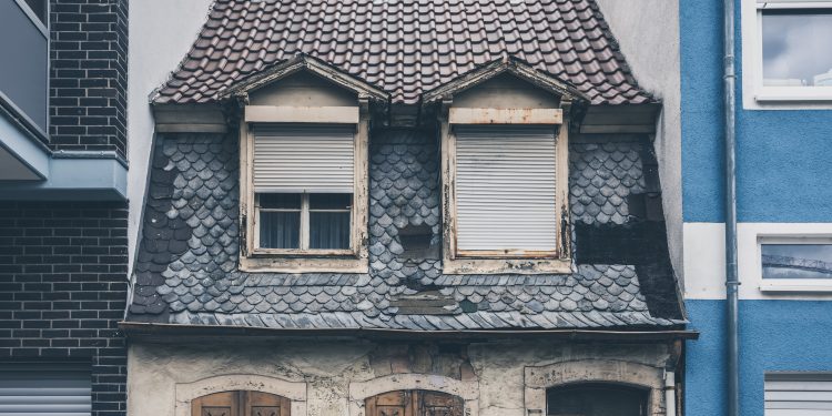 A small aged and old house between two modern and new houses