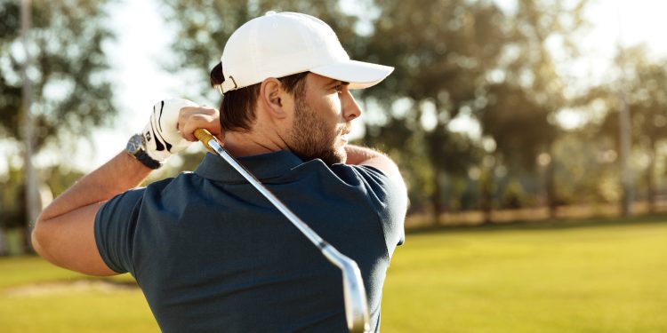 Close up of a young concentrated man shooting golf ball while playing at the green course