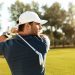 Close up of a young concentrated man shooting golf ball while playing at the green course