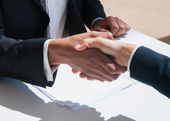 Closeup of business people shaking hands outdoors. Business man and woman wearing formal clothes and sitting at table with papers. Agreement concept.