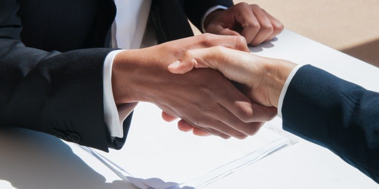 Closeup of business people shaking hands outdoors. Business man and woman wearing formal clothes and sitting at table with papers. Agreement concept.