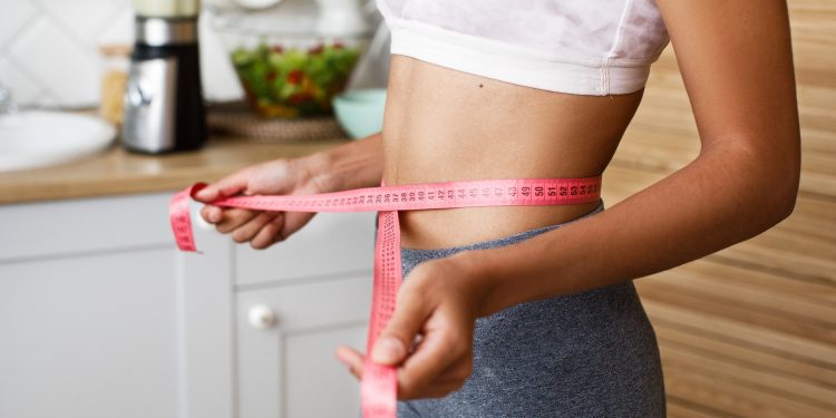 African woman is measuring her waist with a centimeter