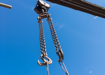 Close-up of a metal chain of a crane lifted up against a clear blue sky at a construction site in working condition for lifting and transporting a heavy load.