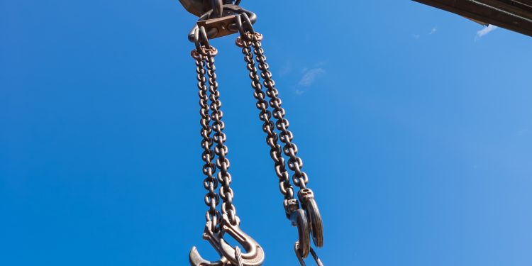 Close-up of a metal chain of a crane lifted up against a clear blue sky at a construction site in working condition for lifting and transporting a heavy load.