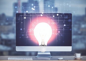 Computer on desktop in office with bulb icon hologram. Multi exposure. Concept of idea.