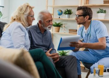 General practitioner showing to senior couple medical documents while being in home visit.