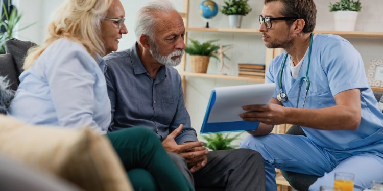 General practitioner showing to senior couple medical documents while being in home visit.