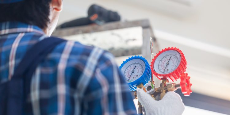 Rear view of Technician man fixing air conditioner unit, Repairman installing air conditioning in a client house, Maintenance and repairing concepts