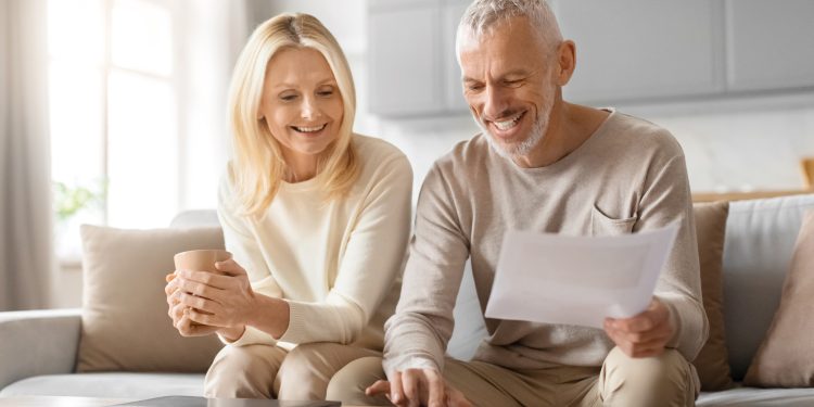A joyful elderly couple engaged in reviewing financial documents while relaxing at home with cups of coffee
