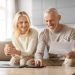 A joyful elderly couple engaged in reviewing financial documents while relaxing at home with cups of coffee