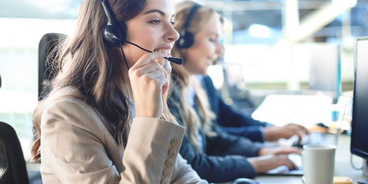 Female customer support operator with headset and smiling, with collegues at background
