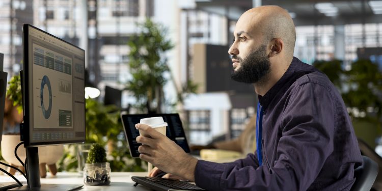 Middle eastern office employee working with monthly revenue balance to create financial plans using online tools, reviewing data analytics. Young businessman manages objectives for success.