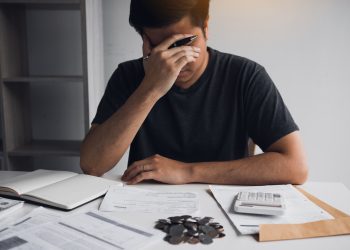 Asian men are stressed about financial problems, with invoices and calculators placed on the table while having stress on problems with home expenses.