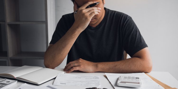Asian men are stressed about financial problems, with invoices and calculators placed on the table while having stress on problems with home expenses.