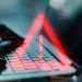 Red exclamation warning symbol overlaying a laptop keyboard with programming code in the background. Concept of software error or digital issue