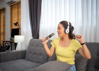 Woman wearing headphones and listening to music and singing happy at home on vacation.