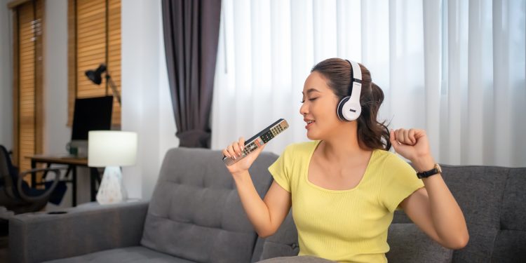 Woman wearing headphones and listening to music and singing happy at home on vacation.