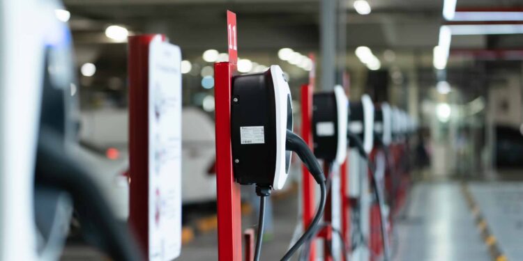 Electric car charging station for charge EV battery. Plug for vehicle with electric engine. EV charger. Clean energy. Charging point at car parking lot. Green power. Future transport technology.