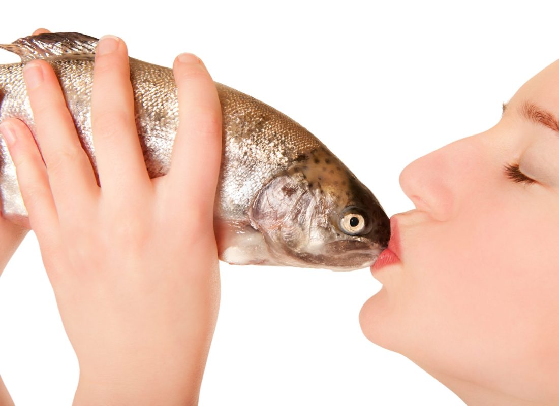 Beautiful young woman kissing a fish