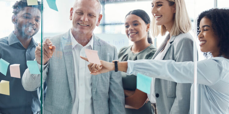 Business people planning on sticky note in meeting, post it paper for creative advertising idea and team collaboration for marketing project. Teamwork for global company strategy on glass in office.