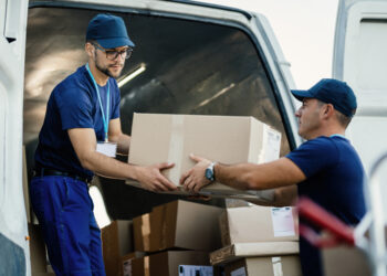 Delivery men loading carboard boxes in a van while getting ready for the shipment.