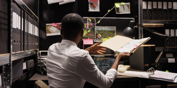 Detective looking at evidence on board and comparing with police report. Investigator holding folder with forensic expertise, analyzing clues and photos attached to office wall