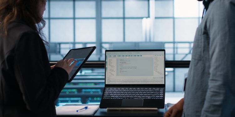 Programmers using AI technology on laptop and tablet in data center employing machine learning models. Devices used by artificial intelligence IT experts in server farm, camera A