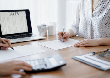 Two accountants using a laptop computer and calculator while counting taxes at wooden desk in office. Teamwork in business audit and finance.