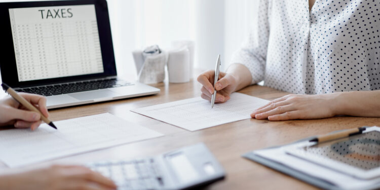 Two accountants using a laptop computer and calculator while counting taxes at wooden desk in office. Teamwork in business audit and finance.