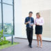 Two confident business colleagues walking on office terrace. Mid adult business man and woman discussing document outdoors on coffee break. Working during break concept