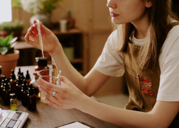 Medium close up of female perfumer adding new essential oil while she preparing new perfume for selling