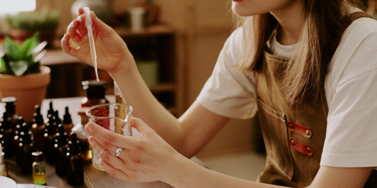 Medium close up of female perfumer adding new essential oil while she preparing new perfume for selling