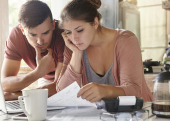 Young female and her unemployed husband with many debts doing paperwork together in kitchen, reading notification, informing that they must move out from their apartment because of non-payment