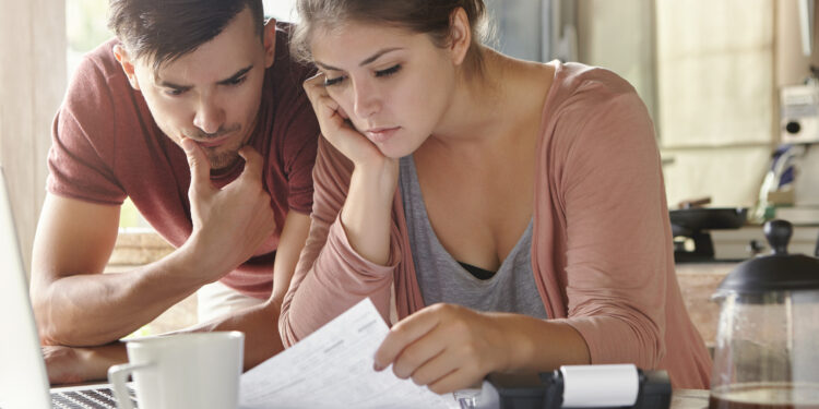 Young female and her unemployed husband with many debts doing paperwork together in kitchen, reading notification, informing that they must move out from their apartment because of non-payment