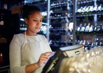 Pretty young cashier registrating orders of clients of cafe, bar or restaurant