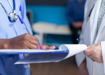 Close up of nurse signing files wtih help from doctor in healthcare cabinet. Medical assistant and specialist holding checkup files to sign for appointment with patient. Woman doing signature