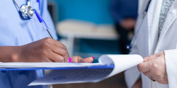 Close up of nurse signing files wtih help from doctor in healthcare cabinet. Medical assistant and specialist holding checkup files to sign for appointment with patient. Woman doing signature