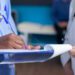 Close up of nurse signing files wtih help from doctor in healthcare cabinet. Medical assistant and specialist holding checkup files to sign for appointment with patient. Woman doing signature