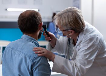 Close up of physician using otoscope to do ear consultation with patient. Woman otologist checking infection with otolaryngology instrument at medical visit during coronavirus pandemic.