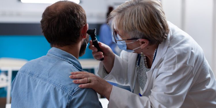 Close up of physician using otoscope to do ear consultation with patient. Woman otologist checking infection with otolaryngology instrument at medical visit during coronavirus pandemic.