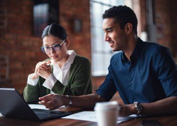 Two individuals seated at a table working together on a laptop, emphasizing teamwork and professionalism.